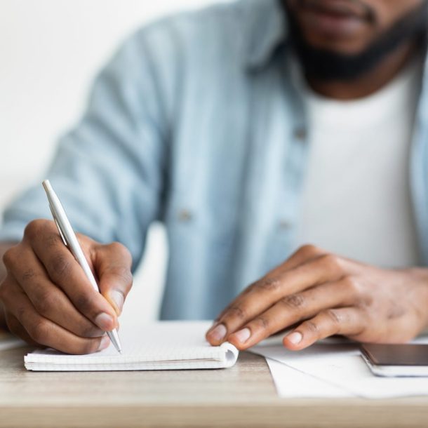 A man writing on a notebook with a pen.