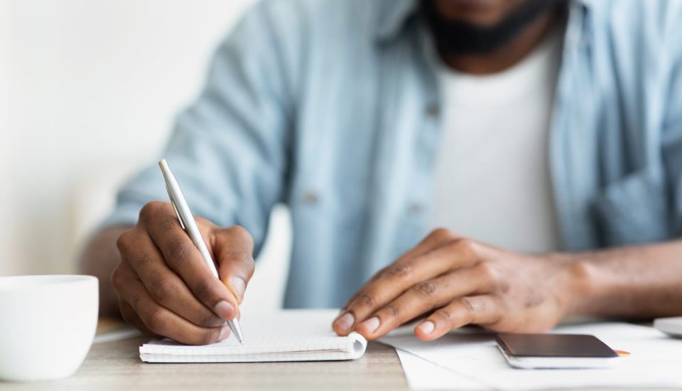 A man writing on a notebook with a pen.