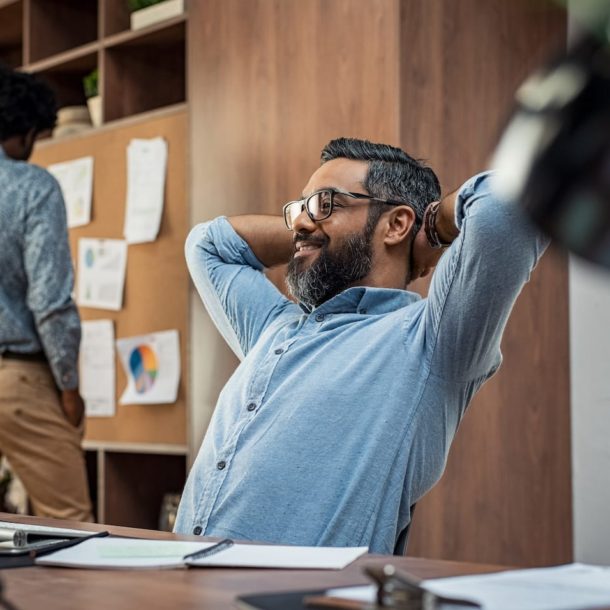 A man sitting at his desk with his hands behind his head.