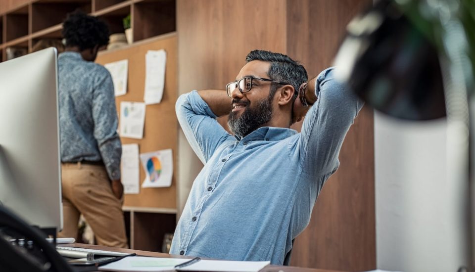 A man sitting at his desk with his hands behind his head.