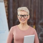 A woman with short hair and glasses holding a laptop.